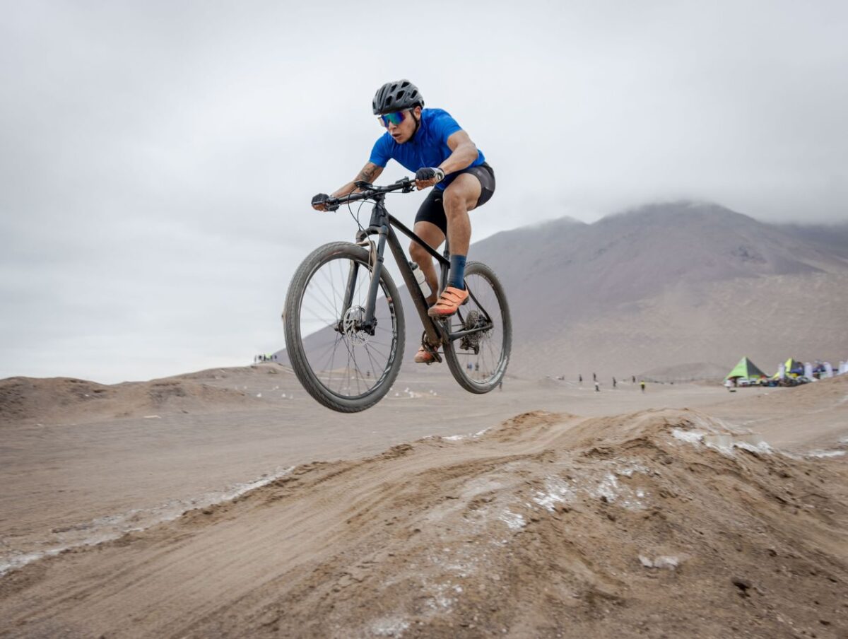 Male cyclist performs a jump on a mountain bike in a desert landscape, showcasing outdoor adventure.