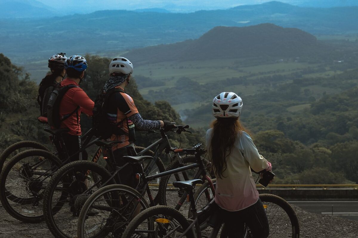 À propos A group of cyclists stand on a hilltop enjoying a breathtaking mountain view, equipped with helmets and bikes.
