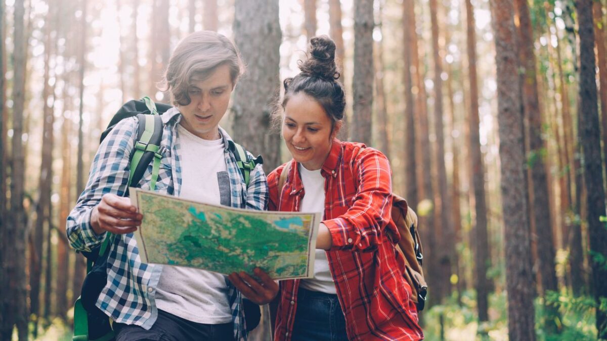Offres A young couple with backpacks exploring a forest using a map. Adventure and travel concept.
