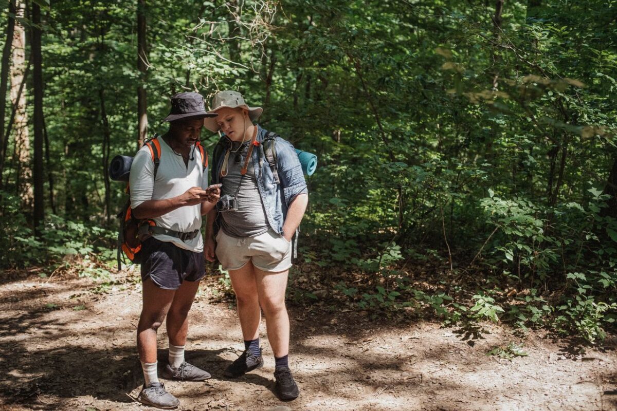 Offres Young multiracial male travelers with rucksacks watching cellphone on pathway against greenery trees in woods