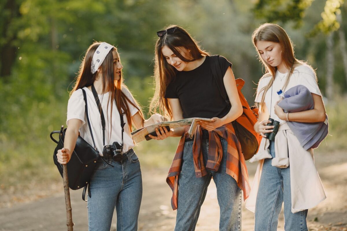 Offres Three young women hiking in a forest while reading a map, enjoying a sunny day.